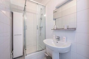 A bathroom with a glass-enclosed shower, a white sink, and a mirror above it. - 2-bedroom near La Défense - Mobility Lease (Levallois-Perret)