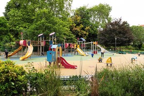 Ein Spielplatz mit verschiedenen Spielgeräten, darunter Rutschen und Kletterbereiche, umgeben von Grünflächen und Bäumen.
