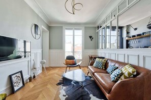 A modern living room with a leather sofa, a flat-screen TV, and a dining area with a kitchen counter. - Chic Parisian 1BR Flat near Montparnasse (Paris)