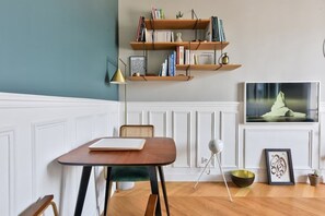A room with a wooden table, a chair, a bookshelf, a framed picture, and a floor lamp. - Chic Parisian 1BR Flat near Montparnasse (Paris)