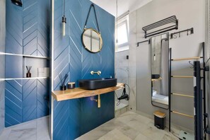 Ein modernes Badezimmer mit blauem geometrischem Wanddesign, einem runden Spiegel, einem schwarzen Waschbecken und einer Duschkabine aus Glas.
