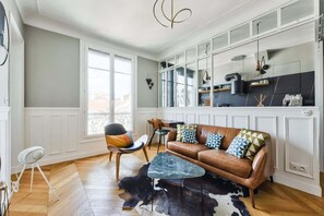 A modern living room with a leather sofa, a coffee table, and a dining area with chairs. - Chic Parisian 1BR Flat near Montparnasse (Paris)