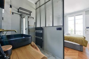 A modern bathroom with a large bathtub, a towel rack, and a mirror. - Chic Parisian 1BR Flat near Montparnasse (Paris)