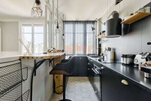 Een moderne keuken met een zwart aanrecht, een houten barstoel en een hangende lamp.