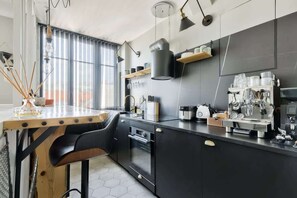 Una cocina moderna con cafetera, barra de madera y armarios negros.