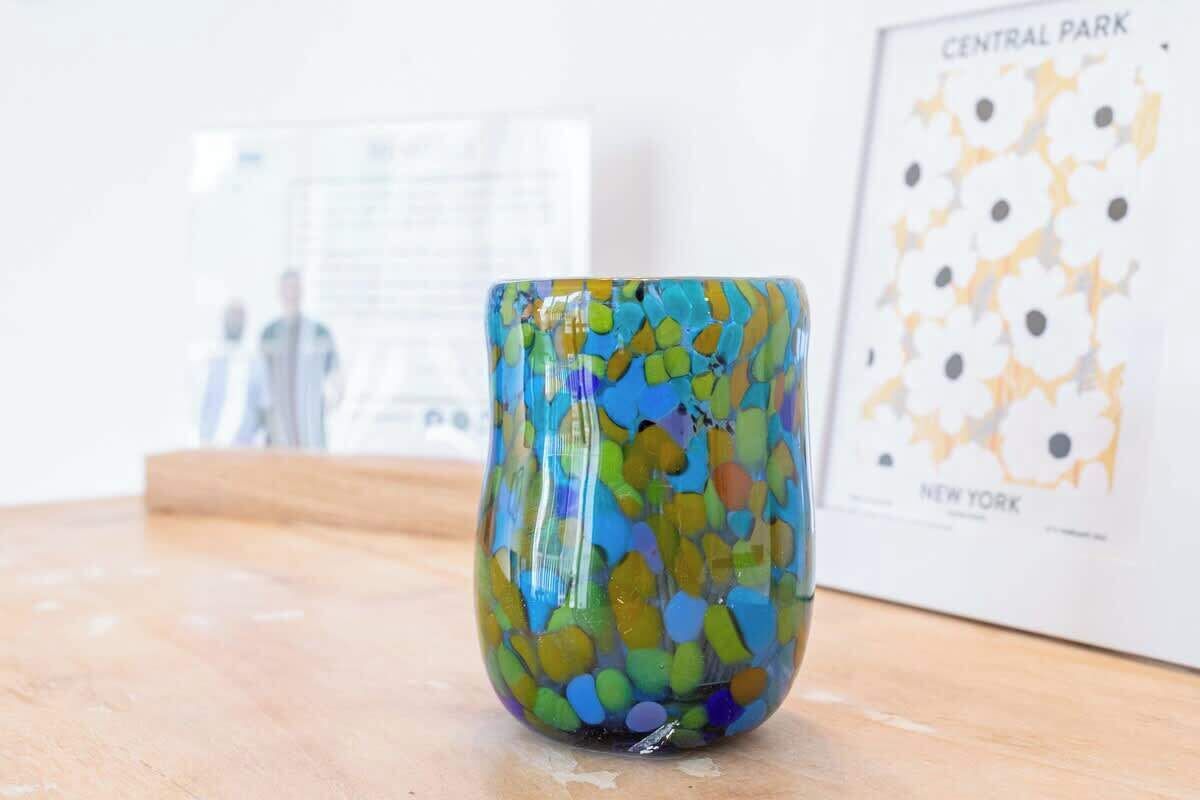 A colorful glass mug on a wooden surface with a framed picture of Central Park in the background.