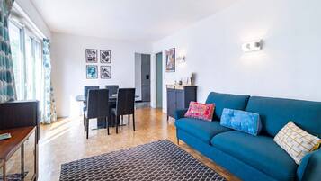 Een moderne woonkamer met een blauwe bank, zwarte stoelen, een houten salontafel en een vloerkleed met een patroon.