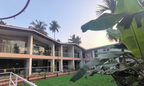 A multi-story building with balconies, a green lawn, and palm trees. - Lexis Inn Beach Resort (Diveagar)