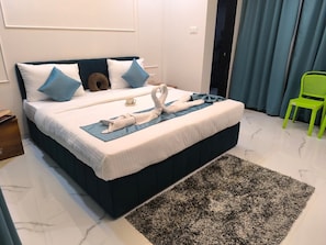 A neatly made bed with pillows, a bedside table, and a green chair. - Lexis Inn Beach Resort (Diveagar)