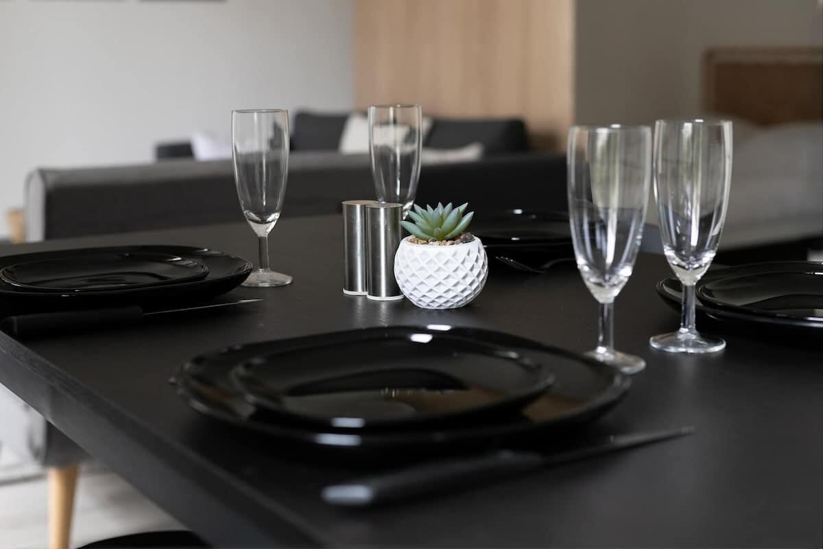 A dining table set with black plates, clear glasses, and a small potted plant.