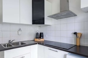 Cozinha moderna com pia de aço inoxidável, fogão por indução preto e armários brancos.
