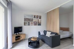 A modern living room with a flat-screen TV, a sofa, a bed, and a wall with multiple photographs. - Cosy Studio - Terrace & Parking - Close to Paris (Le Bourget)