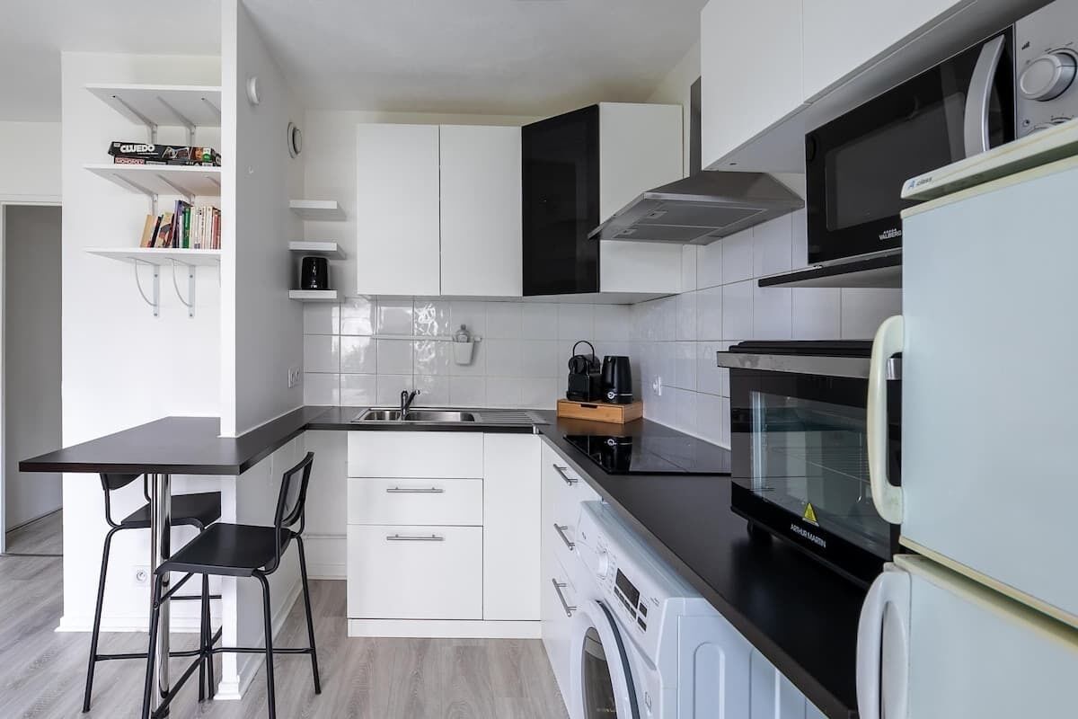 A modern kitchen with white cabinetry, a black countertop, a built-in washing machine, and a microwave.