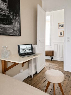 Ein Zimmer mit einem weißen Heizkörper, einem Laptop auf einem weißen Tisch, einer Bank und einer Tür zu einem anderen Raum.