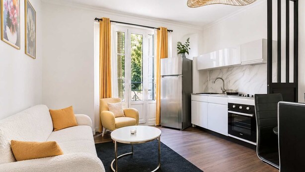 Una sala de estar moderna con un sofá, una mesa de centro y una zona de cocina con armarios y electrodomésticos.