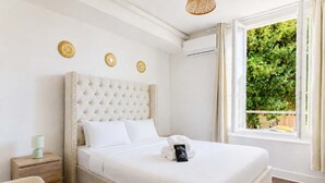 Habitación de hotel con una cama grande, una mesita de noche, una lámpara y una ventana con vista a follaje.