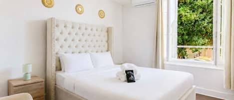 A hotel room with a large bed, a bedside table, a lamp, and a window with a view of greenery.