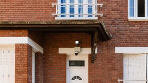Un edificio de ladrillo de dos pisos con una puerta frontal blanca, un balcón pequeño y una serie de escalones de concreto que conducen a la entrada.
