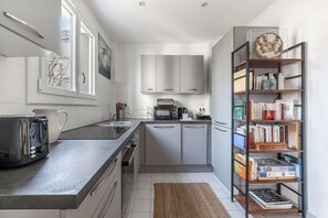 A modern kitchen with a central island, a built-in oven, and a bookshelf filled with books. - Spacious fully equipped 1-bedroom - Mobility lease (Paris)