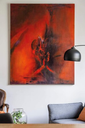 Una habitación con un cuadro abstracto grande, una lámpara moderna, un sofá y una mesita con una planta.