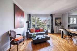 A modern living room with a sofa, coffee table, and a dining area with chairs. - Spacious fully equipped 1-bedroom - Mobility lease (Paris)