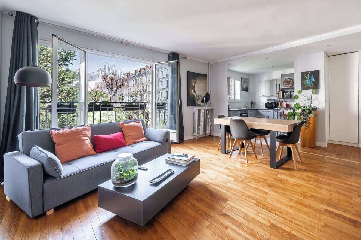 A modern living room with a grey sofa, a coffee table with a glass jar, and a dining area with a wooden table and chairs.