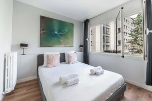 A hotel room with a bed, a radiator, a painting, and a window with curtains. - Spacious fully equipped 1-bedroom - Mobility lease (Paris)