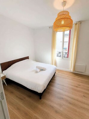 Ein Schlafzimmer mit einem Bett, Holzboden, einem Fenster mit Vorhängen und einer Pendelleuchte.