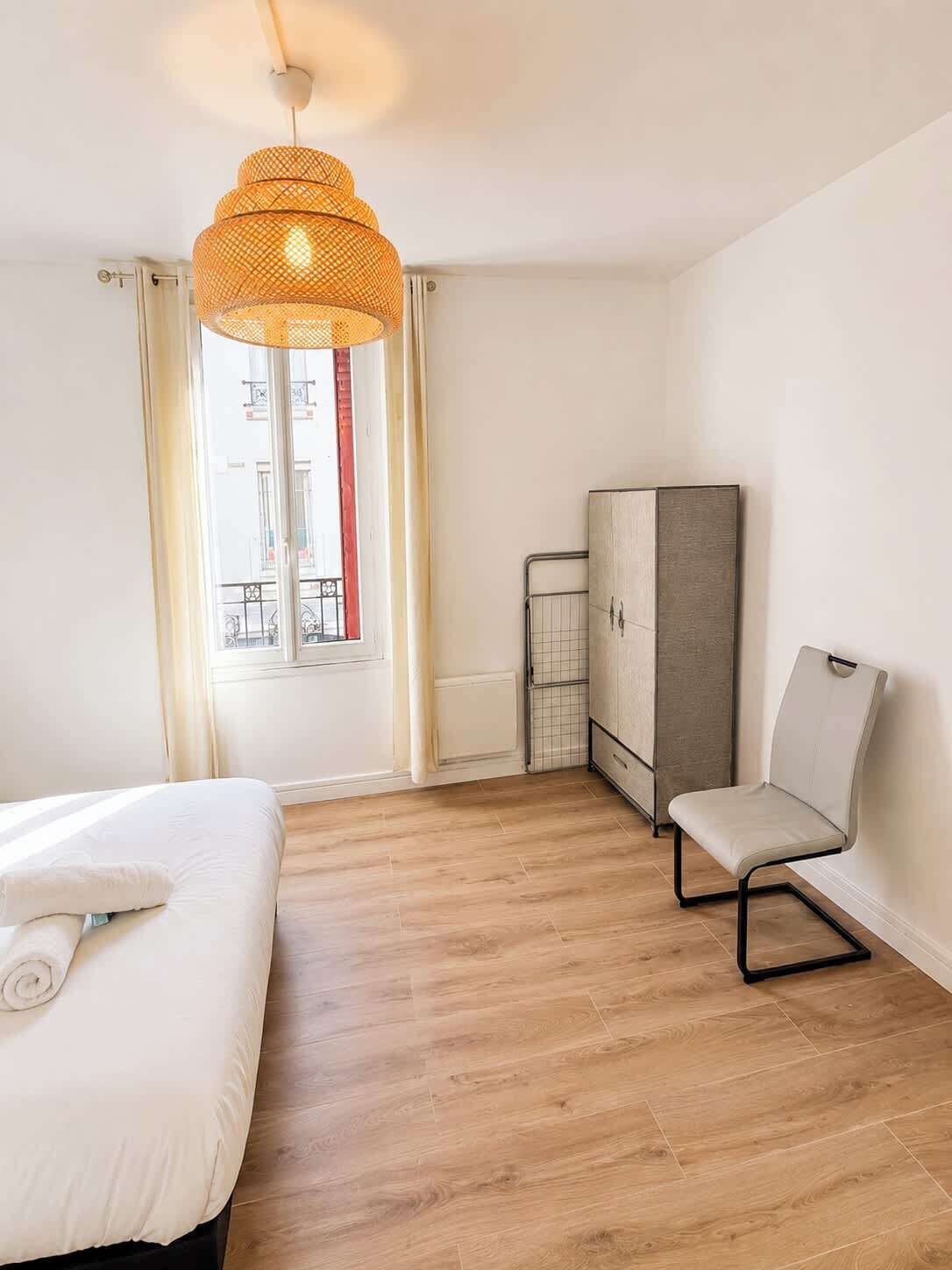 A hotel room with a bed, a chair, a wardrobe, and a hanging light fixture.