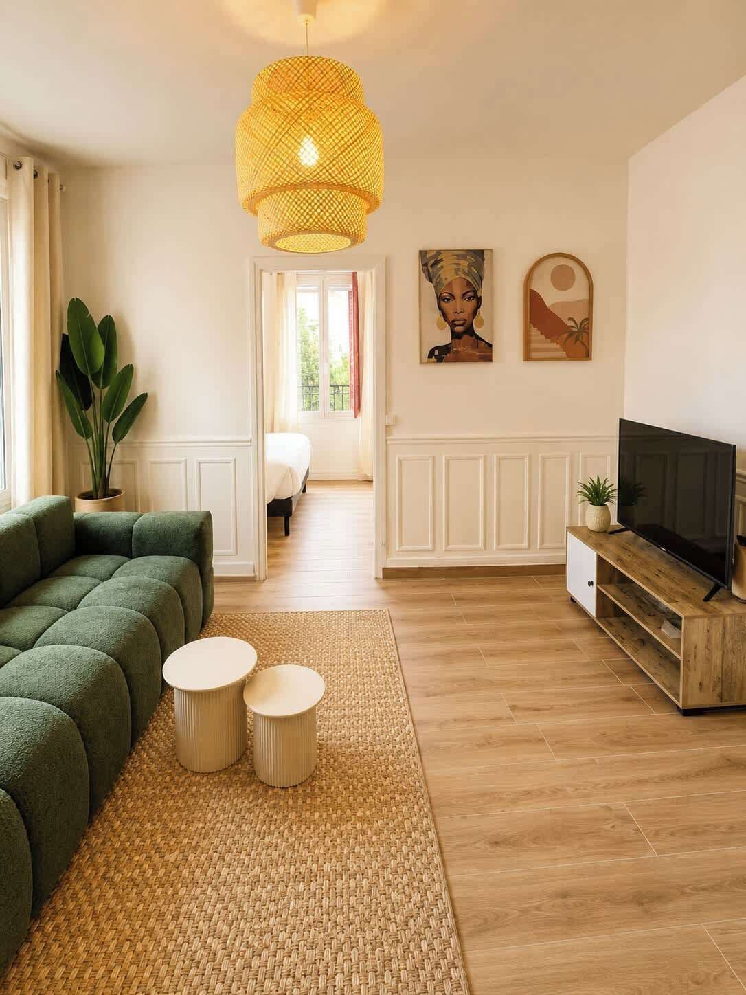 A modern living room with a green sofa, two round side tables, a TV on a wooden stand, and a large woven pendant light.