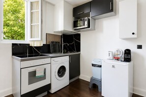 A compact kitchen with a built-in washing machine, a microwave, and a coffee machine. - Beau pavillon climatisé/ Parking (Le Bourget)