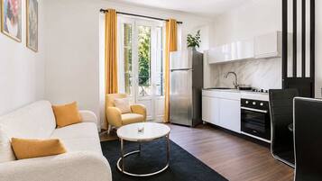 A modern living room with a sofa, a coffee table, and a kitchen area with cabinets and appliances.