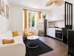 A modern living room with a sofa, a coffee table, and a kitchen area with cabinets and appliances. - Beau pavillon climatisé/ Parking (Le Bourget)