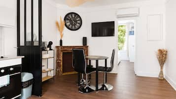 A modern kitchen with a black stove, a dining area with a round table and black chairs, a black clock on the wall, and a large window.