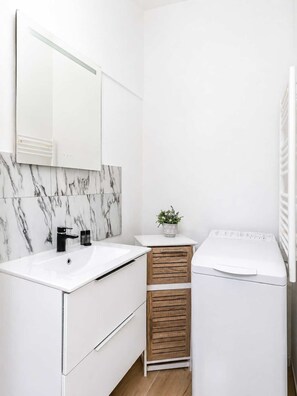 Un bany modern amb un lavabo blanc, un mirall, una resclosa de marbre, un armari de fusta i una rentadora blanca.