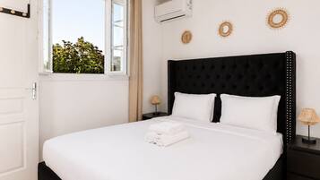 A bedroom with a black headboard, white bedding, and a window with a view of greenery.