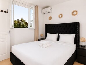 A bedroom with a black headboard, white bedding, and a window with a view of greenery. - Beau pavillon climatisé/ Parking (Le Bourget)