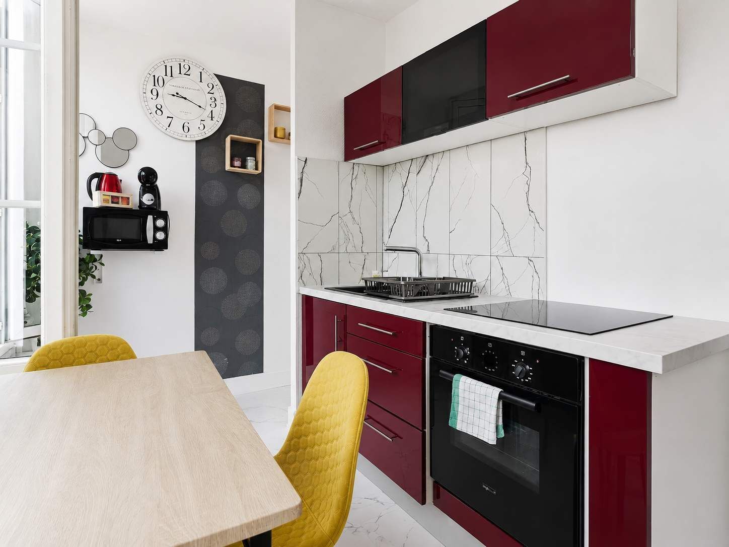A modern kitchen with a black stove, red cabinets, and a white countertop.