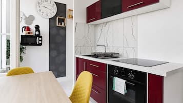 A modern kitchen with a black stove, red cabinets, and a white countertop.