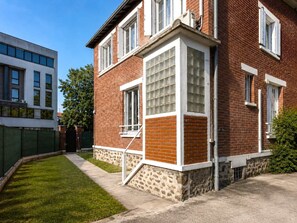 A two-story brick building with a stone base, large windows, and a visible staircase. - Havre cosy climatisé - Parking (Le Bourget)