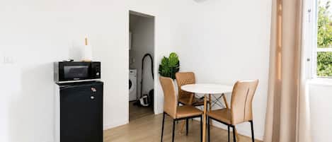 A compact living space with a kitchenette, a dining area with a round table and chairs, and a window with curtains.