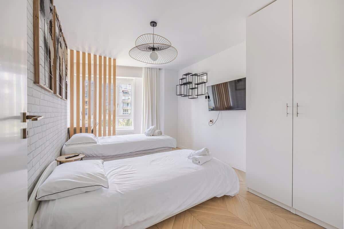 A hotel room with two beds, a TV mounted on the wall, a ceiling fan, and a window with blinds.