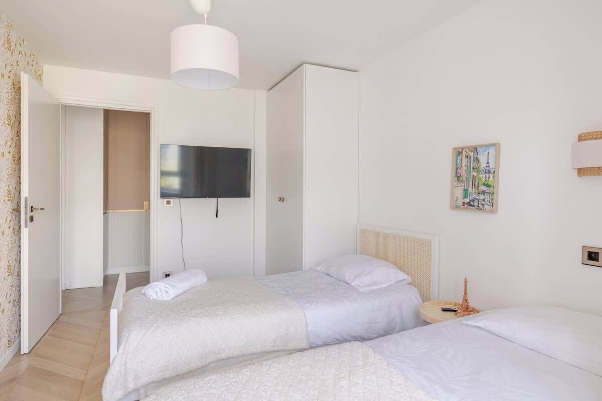A hotel room with two beds, a television, a painting, and a door leading to another room.