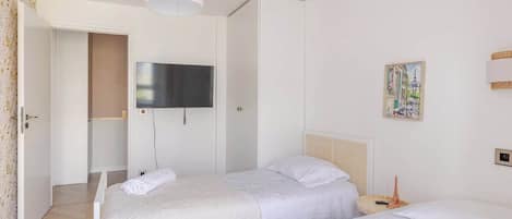 Een hotelkamer met twee bedden, een televisie, een schilderij en een deur naar een andere kamer.