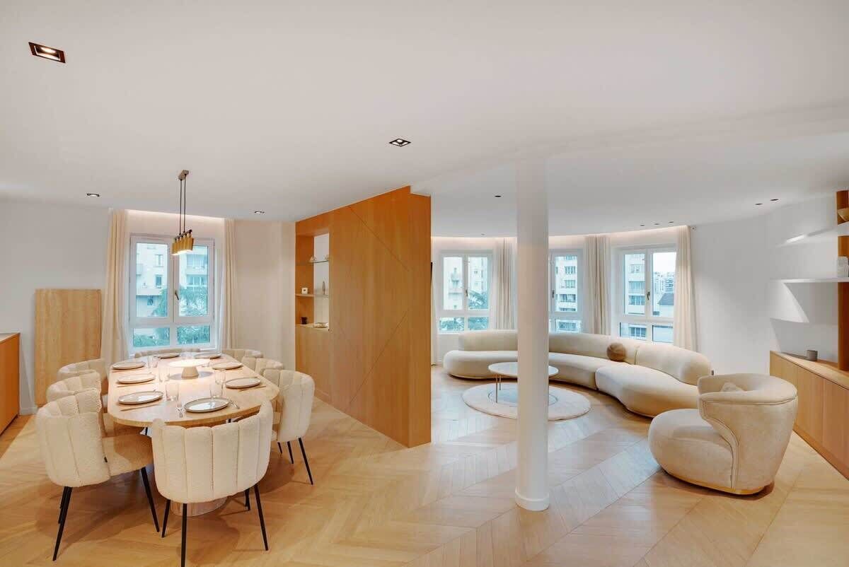 Un salon moderne comprenant un coin repas, un canapé incurvé et une grande fenêtre laissant entrer la lumière naturelle.