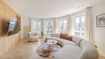 Ein modernes Wohnzimmer mit einer gebogenen Couch, einem runden Couchtisch und einem flachbildfernseher an der Wand.