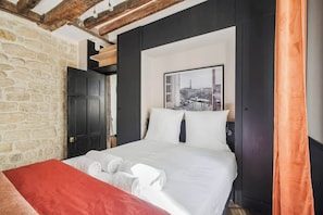 Hotelkamer met een stenen muur, een bed met witte lakens, een rode plaid en een lijst met een foto.