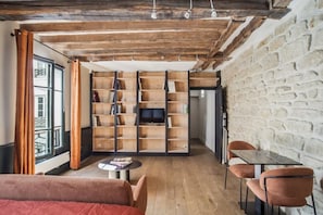 A cozy room with a wooden bookshelf, a TV, a dining table, and a sofa. - Fully Equipped Studio – Concorde – Mobility Lease (Paris)