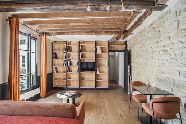 Een gezellige kamer met een houten boekenkast, een televisie, een eettafel en een bank.