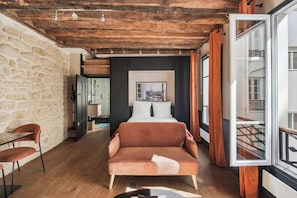 A cozy room with a wooden ceiling, a bed, a sofa, and a dining area with chairs. - Fully Equipped Studio – Concorde – Mobility Lease (Paris)